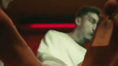 A Man In A White Shirt Is Sitting In A Chair In A Dark Room With His Legs Crossed . GIF