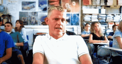 A Man In A White Shirt Is Sitting In A Classroom With A Group Of Students . GIF