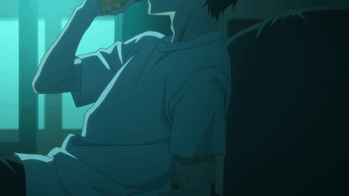 A Man In A White Shirt Is Sitting In A Dark Room Drinking From A Bottle GIF