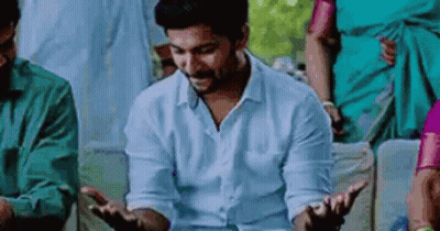 A Man In A White Shirt Is Sitting In A Stadium With His Hands Outstretched And A Group Of People Behind Him . GIF