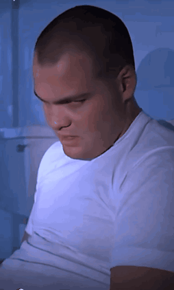 A Man In A White Shirt Is Sitting In Front Of A Blue Wall GIF