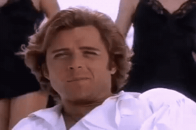 A Man In A White Shirt Is Sitting In Front Of A Group Of Women And Smiling . GIF
