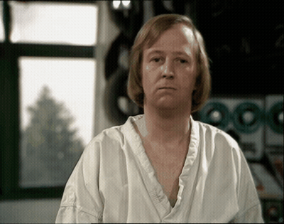 A Man In A White Shirt Is Sitting In Front Of A Laundry Machine GIF