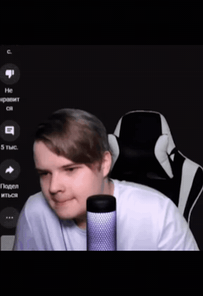 A Man In A White Shirt Is Sitting In Front Of A Microphone With A Black And White Chair Behind Him GIF