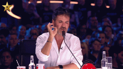 A Man In A White Shirt Is Sitting In Front Of A Microphone With A Gold Star Above Him GIF