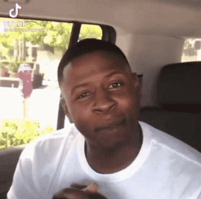 A Man In A White Shirt Is Sitting In The Back Seat Of A Car And Making A Face . GIF