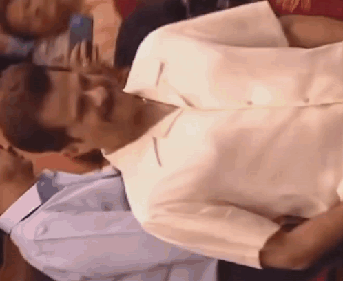 A Man In A White Shirt Is Sitting Next To Another Man In A Blue Shirt . GIF