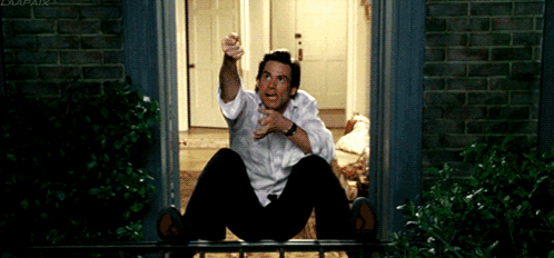 A Man In A White Shirt Is Sitting On A Balcony Pointing GIF