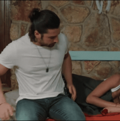 A Man In A White Shirt Is Sitting On A Bed GIF