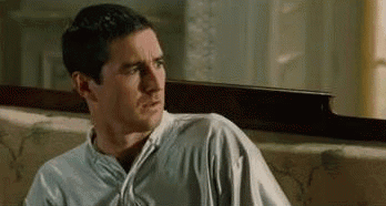 A Man In A White Shirt Is Sitting On A Couch And Looking At Something . GIF