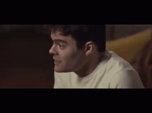 A Man In A White Shirt Is Sitting On A Couch And Looking At Something . GIF