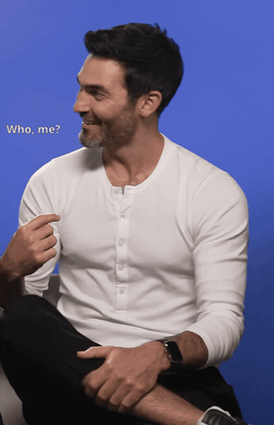 A Man In A White Shirt Is Sitting On A Couch Talking To Another Man With The Words " Who Me " Written Below Him GIF