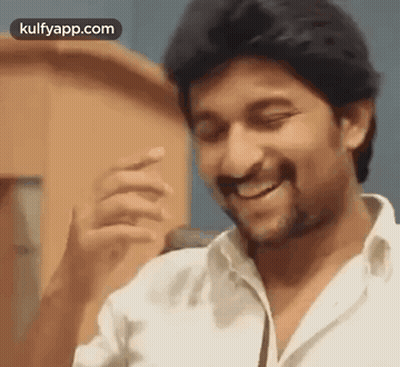 A Man In A White Shirt Is Smiling And Laughing While Standing In Front Of A Microphone . GIF