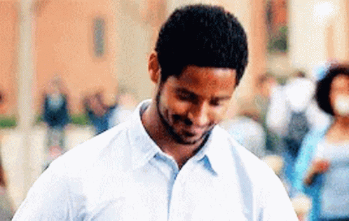 A Man In A White Shirt Is Smiling And Looking Down At Something . GIF