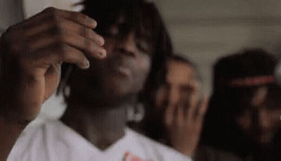 A Man In A White Shirt Is Smoking A Cigarette In A Room . GIF