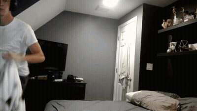 A Man In A White Shirt Is Standing In A Bedroom GIF