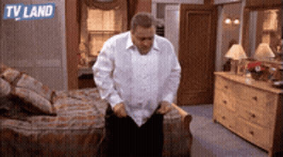 A Man In A White Shirt Is Standing In A Bedroom With A Tv Land Logo On The Wall GIF
