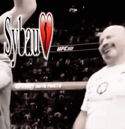 A Man In A White Shirt Is Standing In A Boxing Ring With A Crowd In The Background . GIF