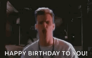 A Man In A White Shirt Is Standing In A Dark Room And Says `` Happy Birthday To You ! '' GIF