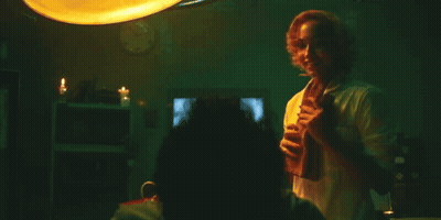 A Man In A White Shirt Is Standing In A Dark Room Holding A Glass Of Wine . GIF