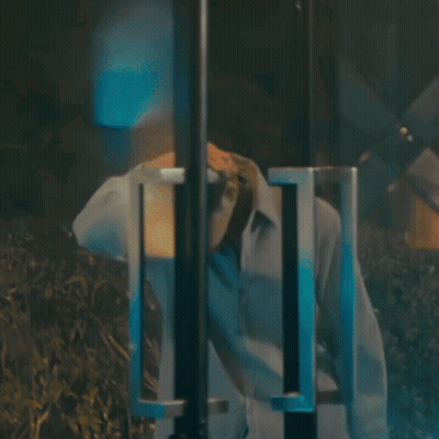 A Man In A White Shirt Is Standing In A Dark Room With His Head Down GIF