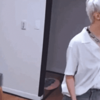 A Man In A White Shirt Is Standing In A Room Next To A Doorway . GIF