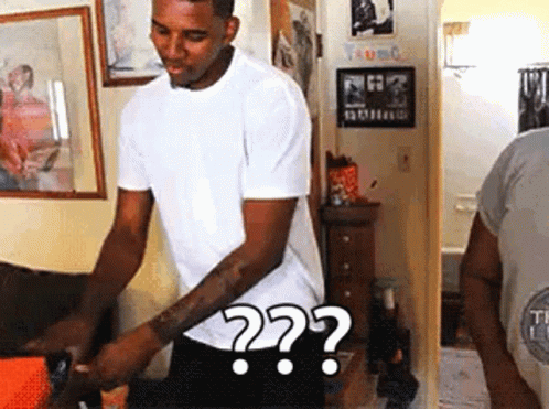 A Man In A White Shirt Is Standing In A Room With A Question Mark . GIF