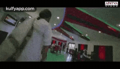 A Man In A White Shirt Is Standing In A Room With A Red And Green Ceiling . GIF