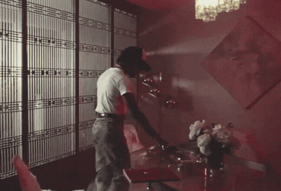 A Man In A White Shirt Is Standing In A Room With A Red Light On The Ceiling GIF