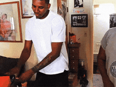 A Man In A White Shirt Is Standing In A Room With A Sign That Says T-Umc GIF
