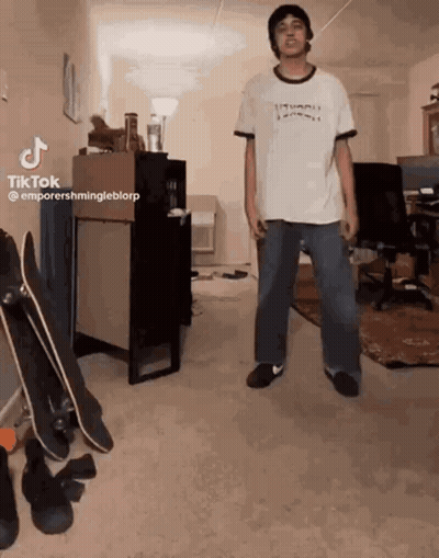 A Man In A White Shirt Is Standing In A Room With Skateboards . GIF