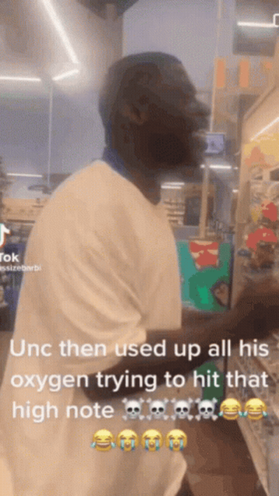 A Man In A White Shirt Is Standing In A Store And Using Oxygen To Try To Hit That High Note . GIF
