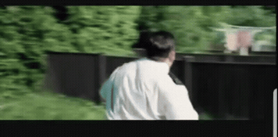 A Man In A White Shirt Is Standing In Front Of A Black Fence . GIF