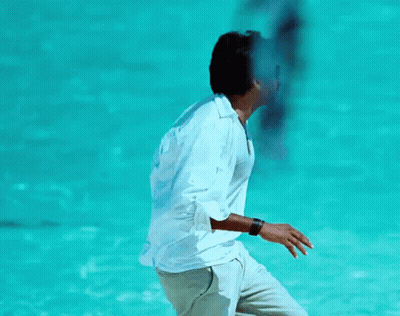 A Man In A White Shirt Is Standing In Front Of A Blue Water GIF