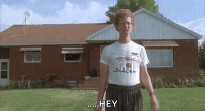 A Man In A White Shirt Is Standing In Front Of A Brick House And Says Hey . GIF