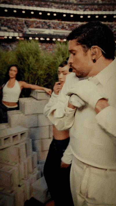 A Man In A White Shirt Is Standing In Front Of A Brick Wall GIF