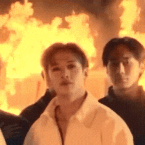A Man In A White Shirt Is Standing In Front Of A Burning Building . GIF