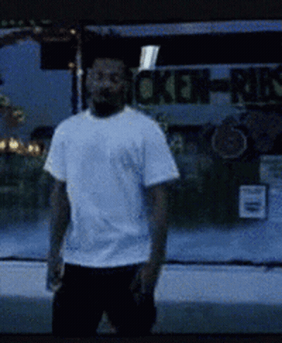 A Man In A White Shirt Is Standing In Front Of A Chicken-Munch Sign GIF