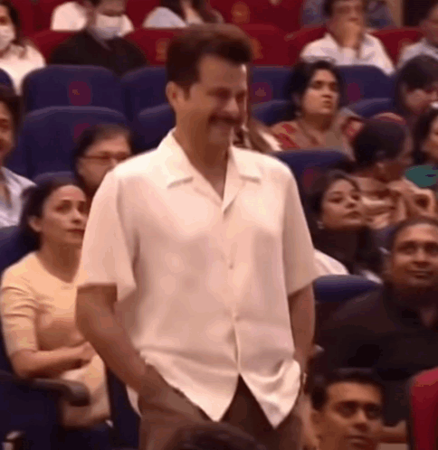 A Man In A White Shirt Is Standing In Front Of A Crowd Of People In An Auditorium . GIF