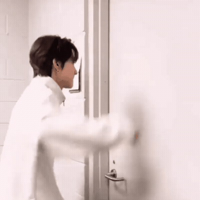 A Man In A White Shirt Is Standing In Front Of A Door . GIF