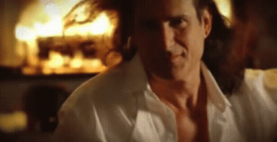 A Man In A White Shirt Is Standing In Front Of A Fire GIF