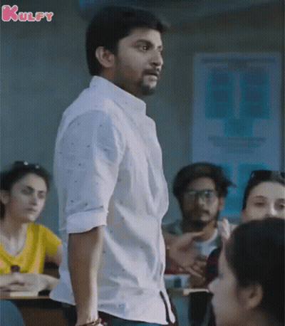 A Man In A White Shirt Is Standing In Front Of A Group Of People In A Classroom With The Word Kulfy On The Bottom GIF