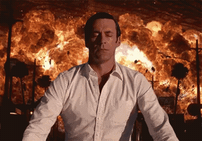 A Man In A White Shirt Is Standing In Front Of A Large Explosion GIF