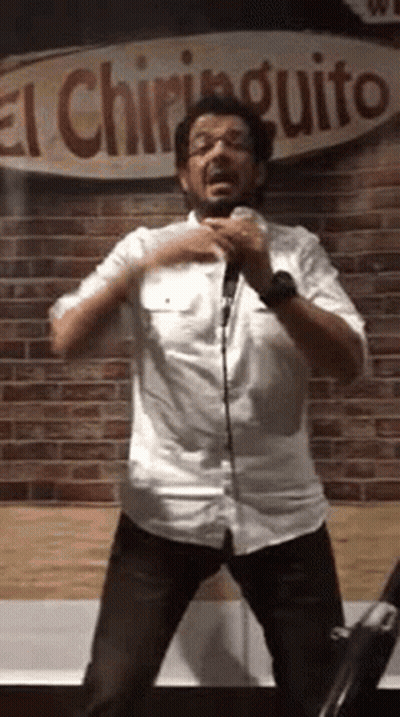 A Man In A White Shirt Is Standing In Front Of A Microphone And Singing Into It . GIF