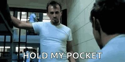 A Man In A White Shirt Is Standing In Front Of A Mirror With The Words `` Hold My Pocket '' Written On It . GIF