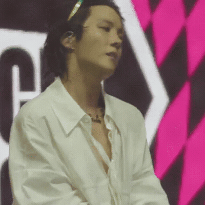 A Man In A White Shirt Is Standing In Front Of A Pink And Black Checkered Wall . GIF