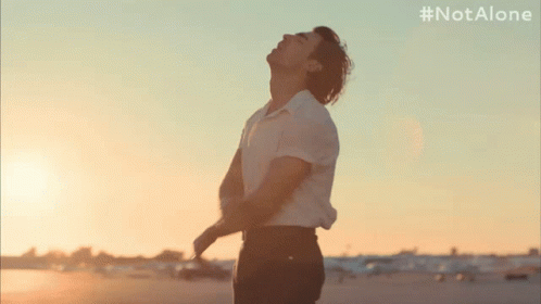 A Man In A White Shirt Is Standing In Front Of A Sunset With The Hashtag #Notalone On The Bottom GIF