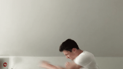 A Man In A White Shirt Is Standing In Front Of A White Wall With A Red Sign That Says ' Aa ' GIF