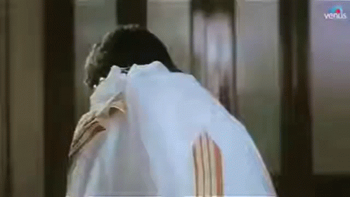 A Man In A White Shirt Is Standing In Front Of A Window And Looking Down . GIF