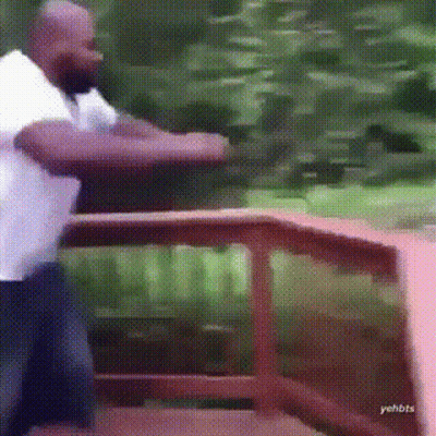 A Man In A White Shirt Is Standing In Front Of A Wooden Railing . GIF